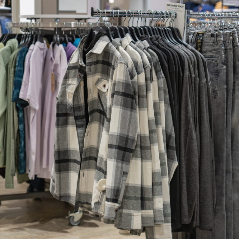 Graue und weiße karierte Hemdjacken hängen nebeneinander an Kleiderbügeln in einem Bekleidungsgeschäft.