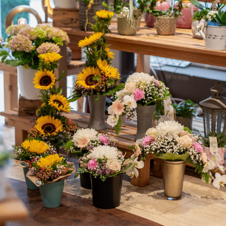 Bunte Blumenarrangements mit Sonnenblumen, Rosen, Nelken und Babys Atem in Töpfen auf Holztischen im Laden.