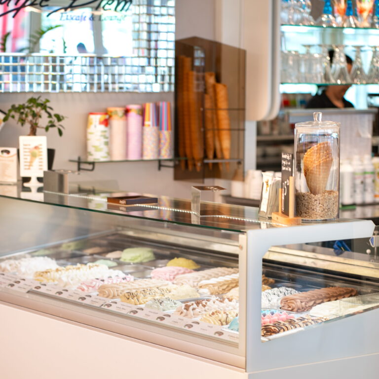 Eisdiele-Theke mit Glasvitrine voller bunter Eissorten und Waffeln in einem Glasbehälter, Thekenbereich unscharf im Hintergrund