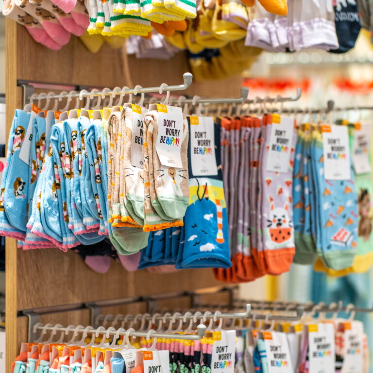 Bunte Socken mit Tier- und Musterprints hängen an Metallstangen in einem Ladengeschäft, Etiketten mit Slogans sichtbar.