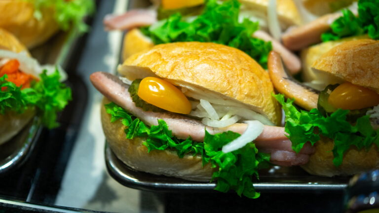 Kleines belegtes Brötchen mit Schinken, Salat, Zwiebeln, Gewürzgurke und gelber Cocktailtomate auf einem Tablett