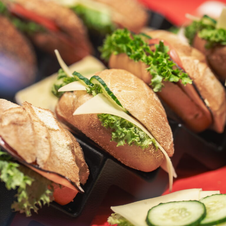 Kleine Brötchen-Sandwiches mit Käse, Gurkenscheiben und frischem grünen Salat in einer Servierschale sichtbar