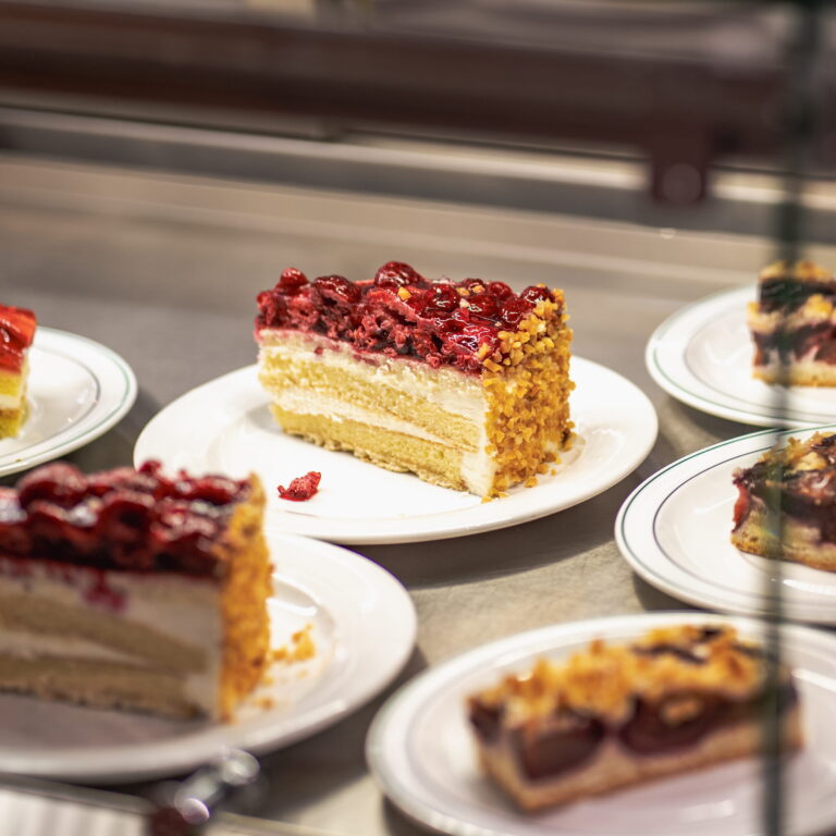 Stück mehrschichtiger Kuchen mit Vanilleböden, Creme, Nussrand und glänzender Kirsch-Fruchtfüllung auf weißem Teller