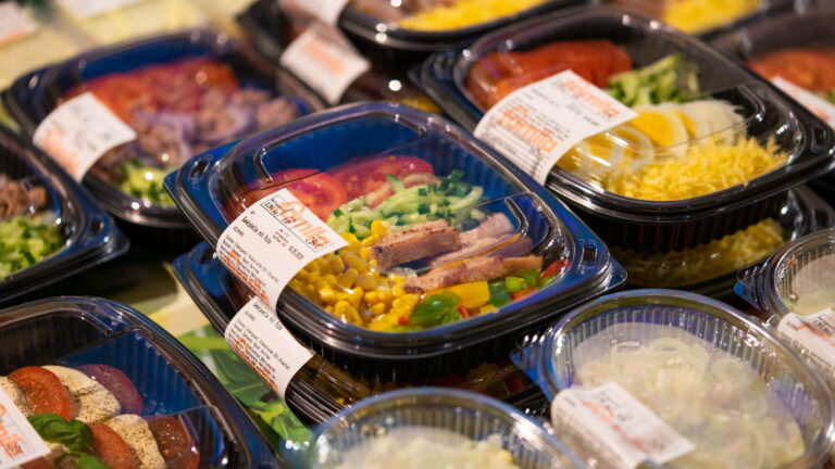 Verschiedene fertig verpackte Salatschalen und Beilagen in Kunststoffbehältern, sichtbar Mais, Gurke, Tomate, Ei und Fleischstücke.