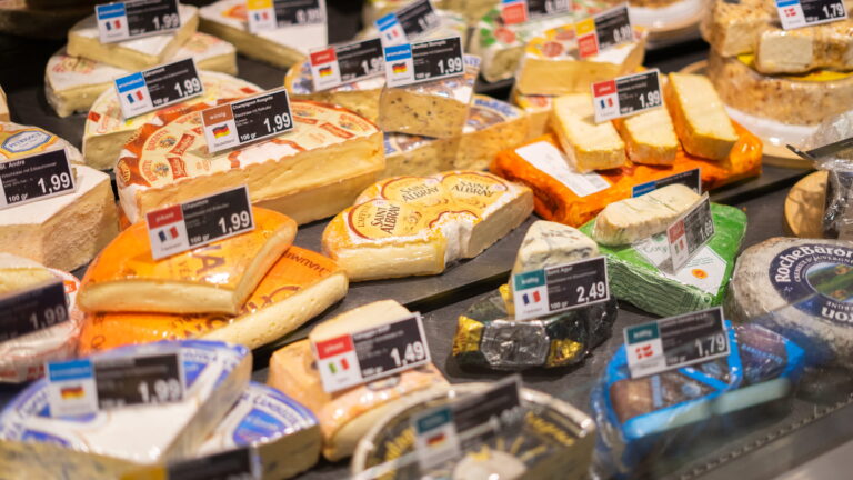 Auslage mit verschiedenen Käsesorten und Preisschildern in einem Lebensmittelladen, u. a. Saint Albray und Blauschimmelkäse.