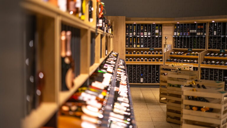 Regalreihen in einem Weinladen mit Holzfächern, vielen liegenden und stehenden Weinflaschen sowie Holzkisten auf dem Boden.