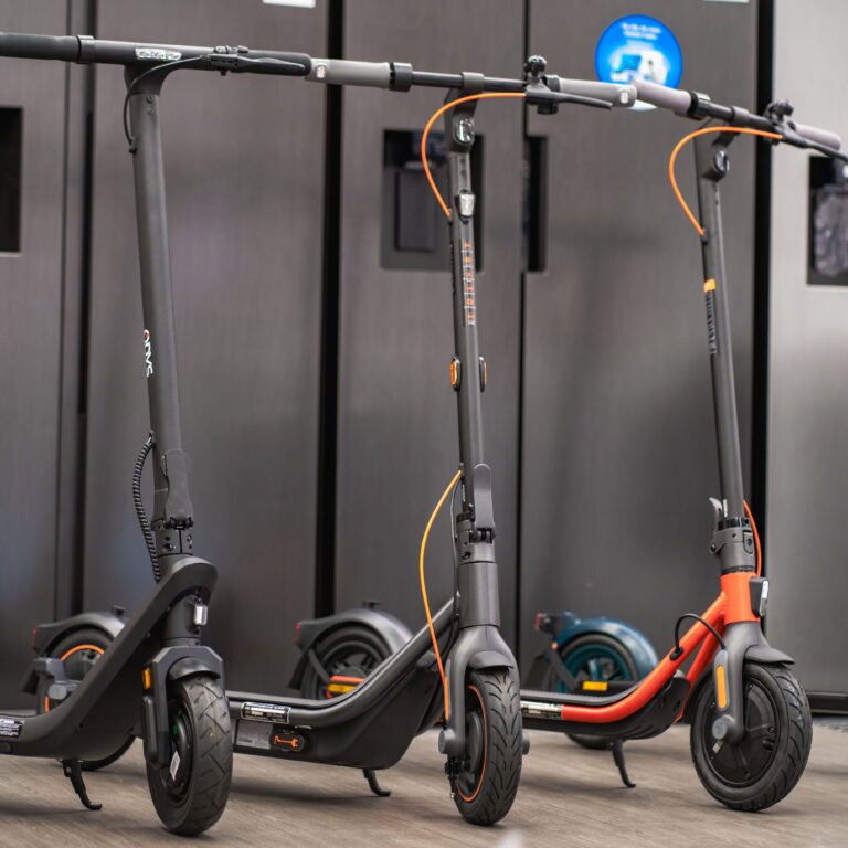 Drei Elektroroller in Reihe, schwarze und ein oranger Rahmen, sichtbare Lenker, Räder und orangefarbene Bremskabel.